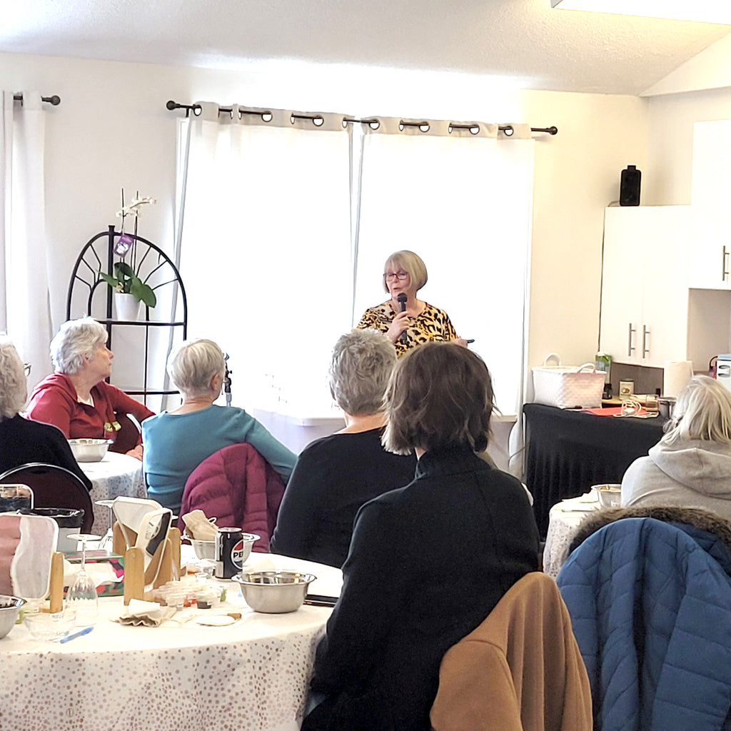 Woman speaking to a group of people in a room with tables and chairs.